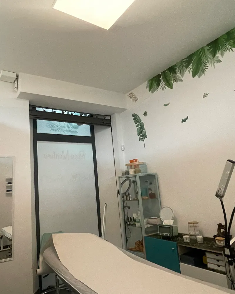 Cabina de tratamiento del centro: camilla, estantería con productos y hojas verdes pintadas en la pared