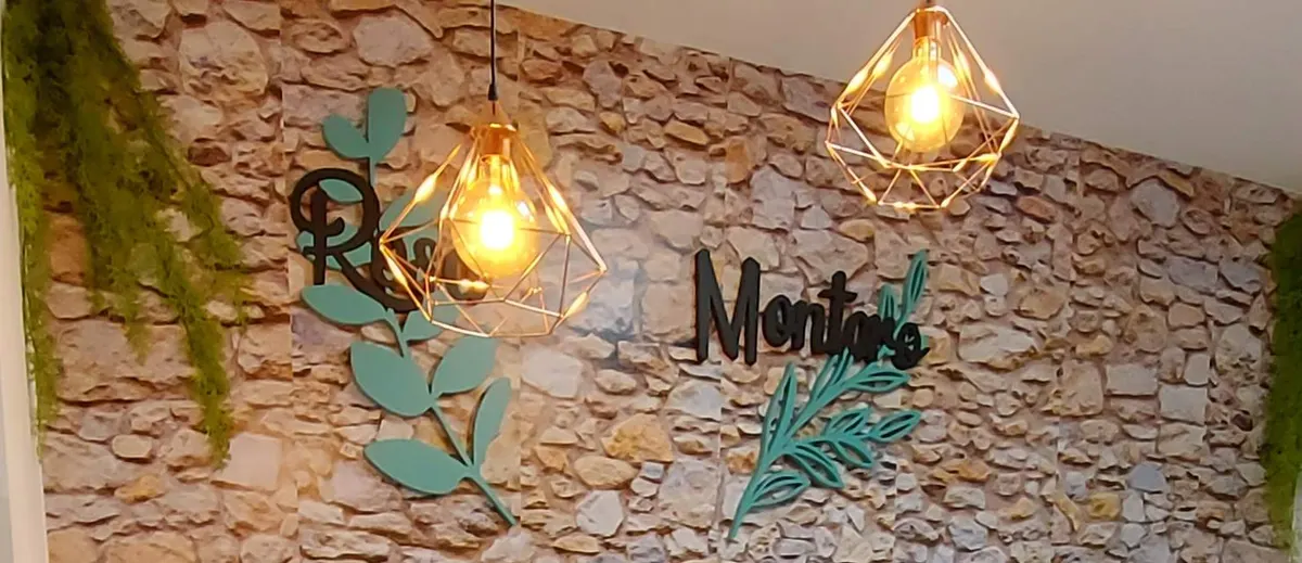 Pared de piedra de la recepción con el logotipo Rosa Montero, ramas verde menta y lámparas doradas
